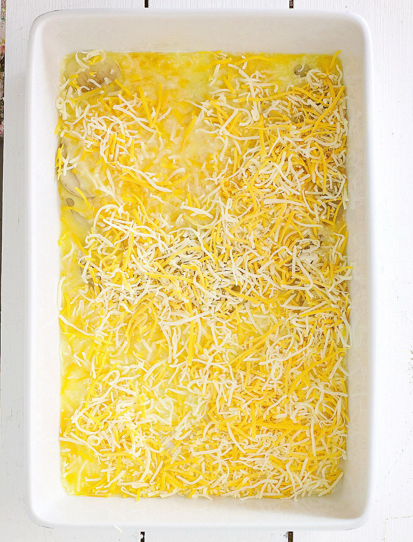shredded cheese over scalloped potatoes casserole ready to go into the oven