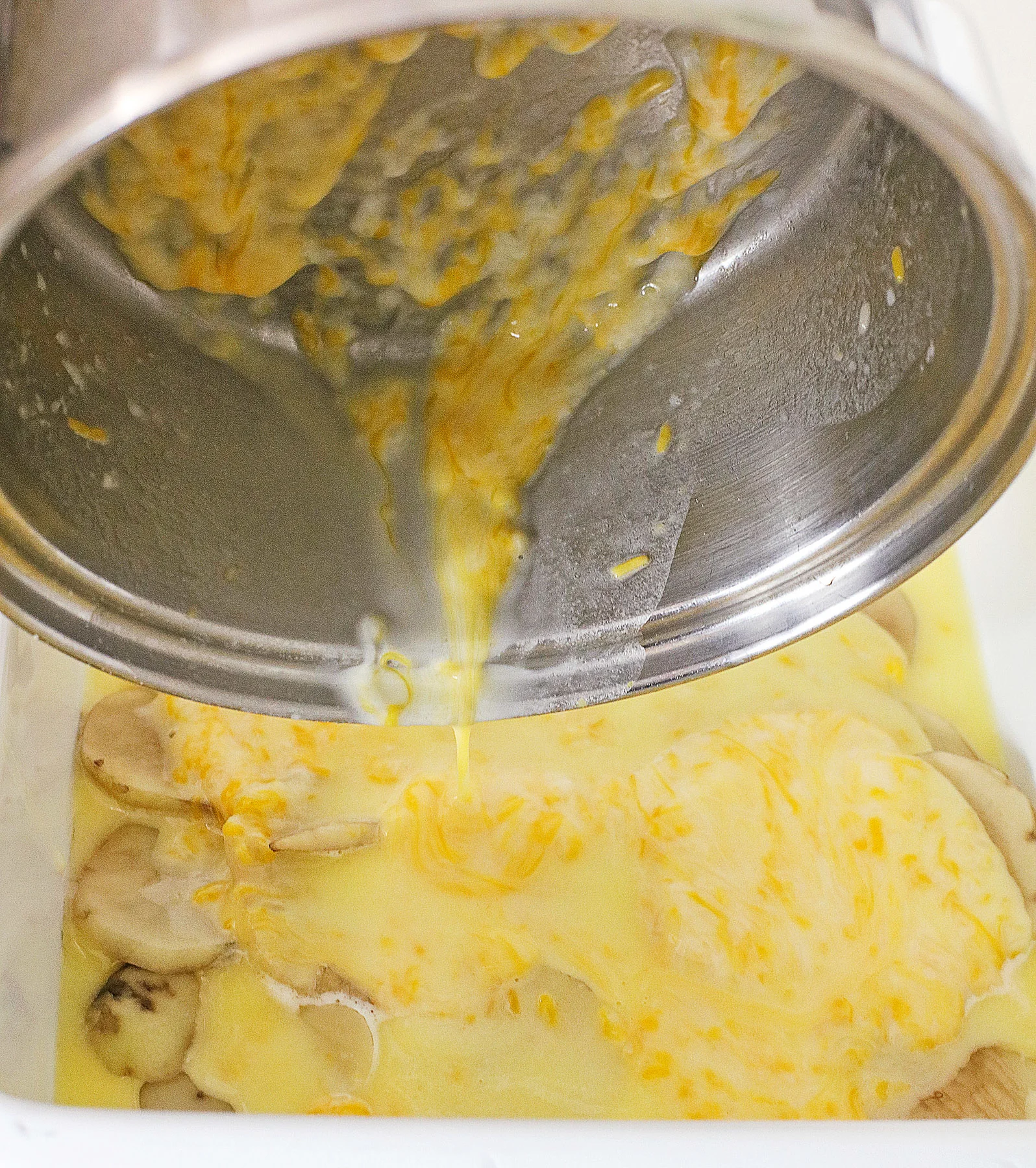pouring butter and cheese mixture onto potato casserole