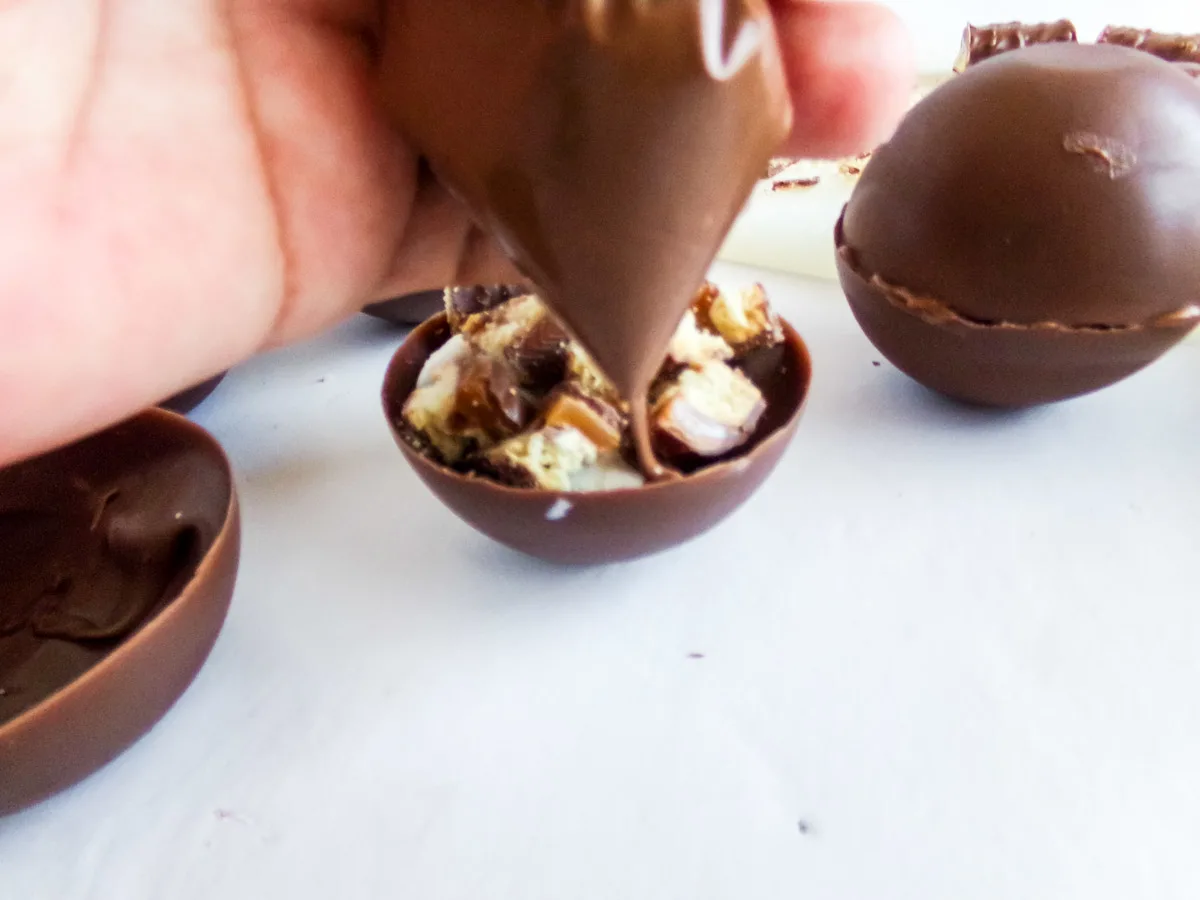 spreading melted chocolate onto a hot cocoa bomb shell