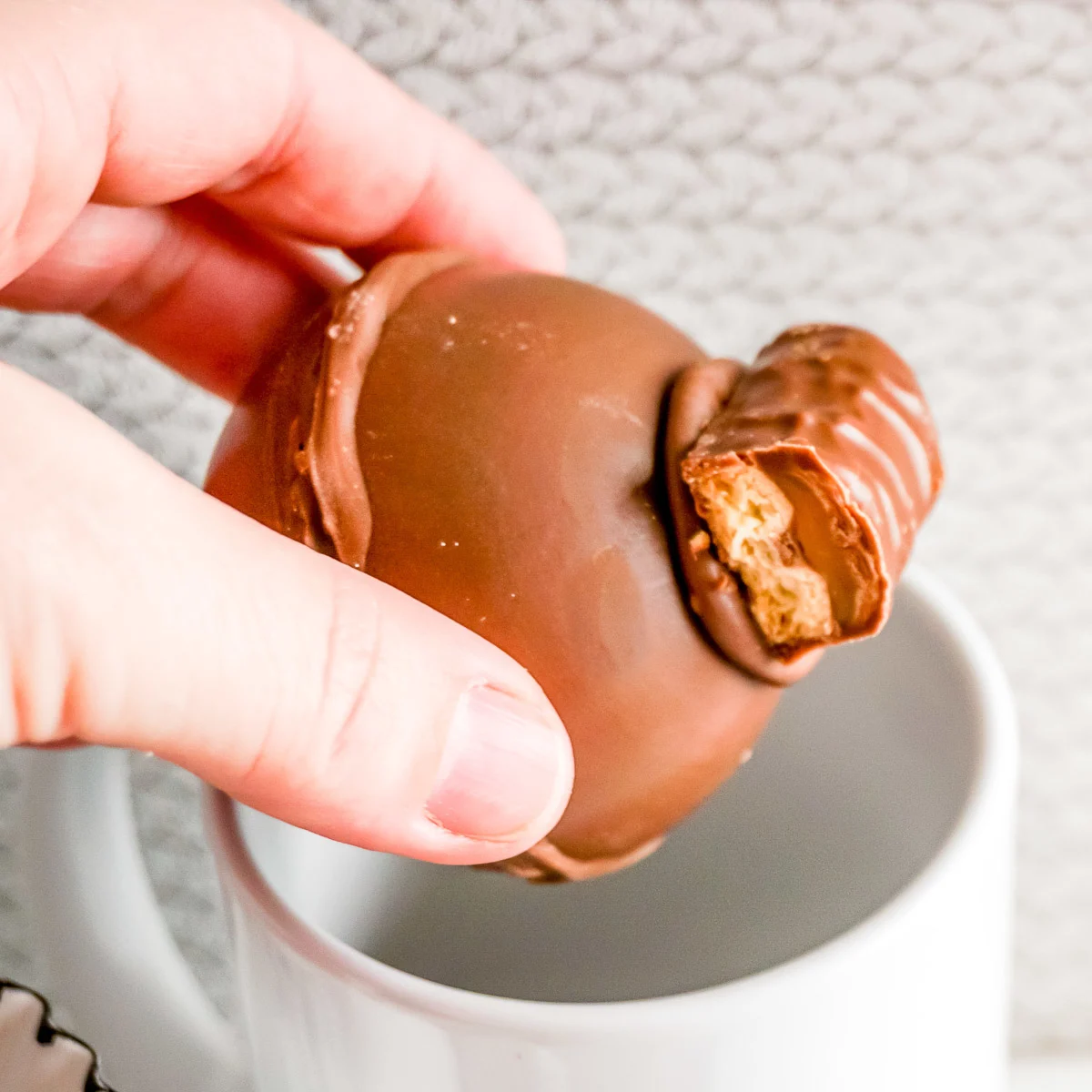 hand placing twix hot cocoa bomb in a mug