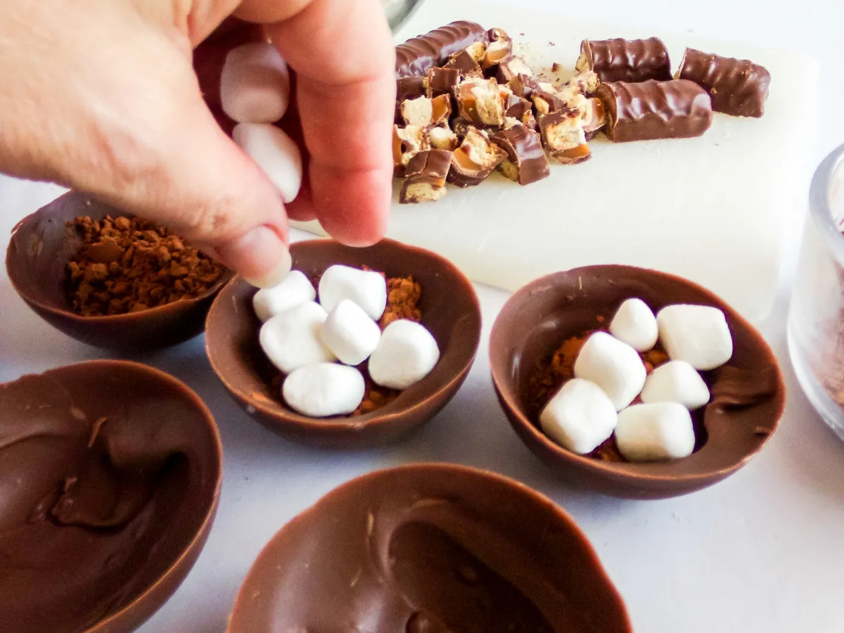 placing hot cocoa and marshmallows into a chocolate candy shell