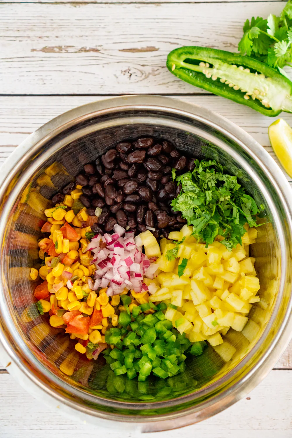 bowl of ingredients to make pineapple black bean salsa: corn, black beans, pineapple, cilantrol, jalapeño, and red onion