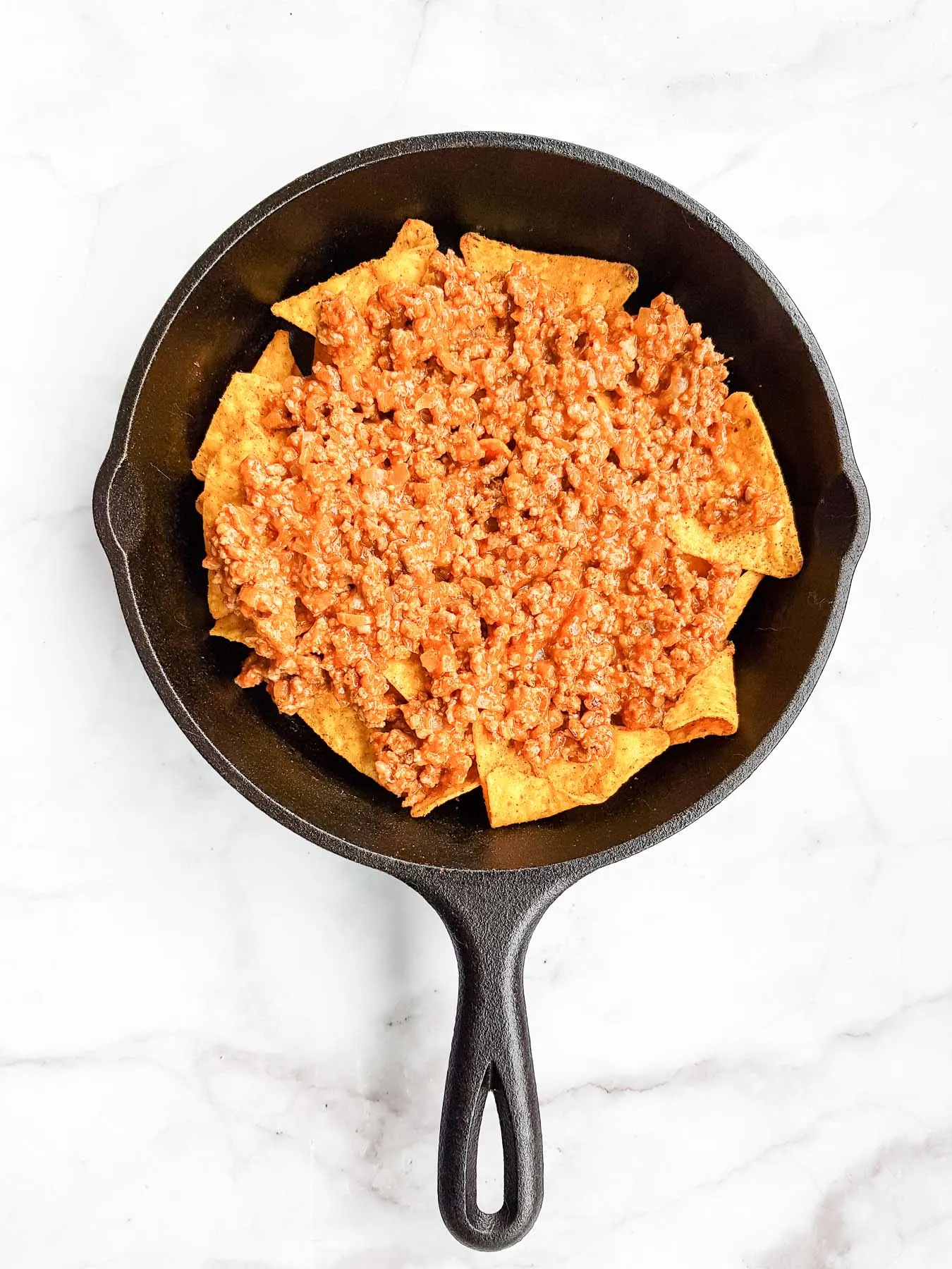 tortilla chips topped with cooked ground beef in a skilet