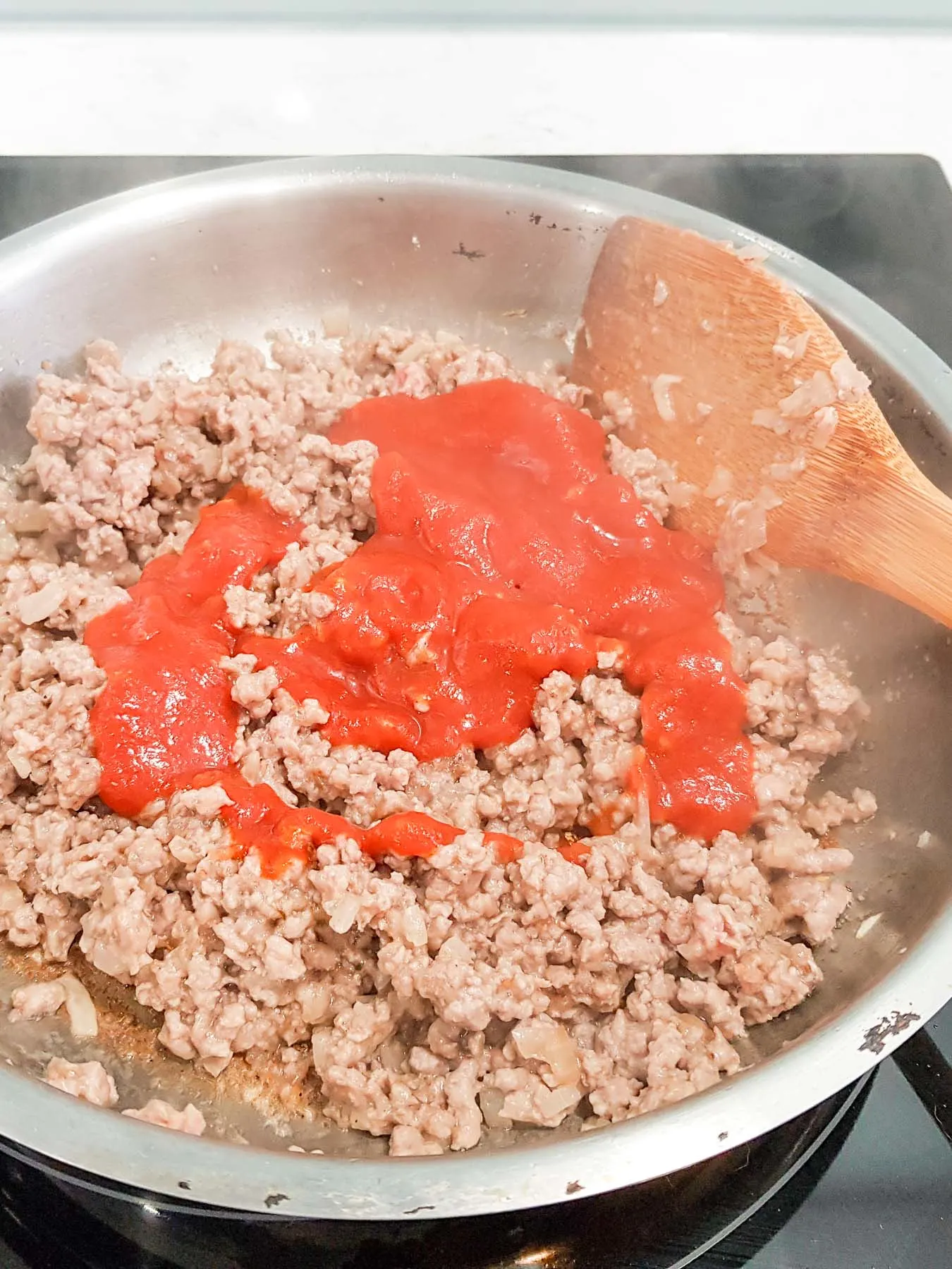adding tomato sauce to ground beef in a skillet