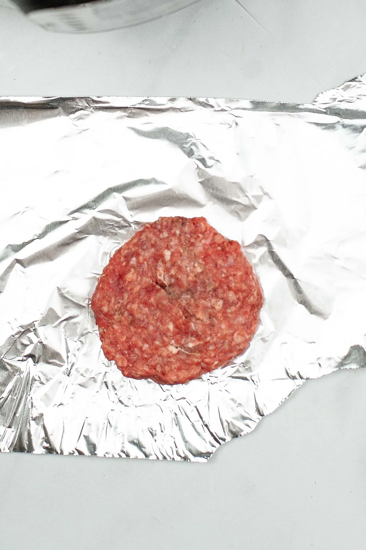 Seasoned ground beef patty on top of foil.