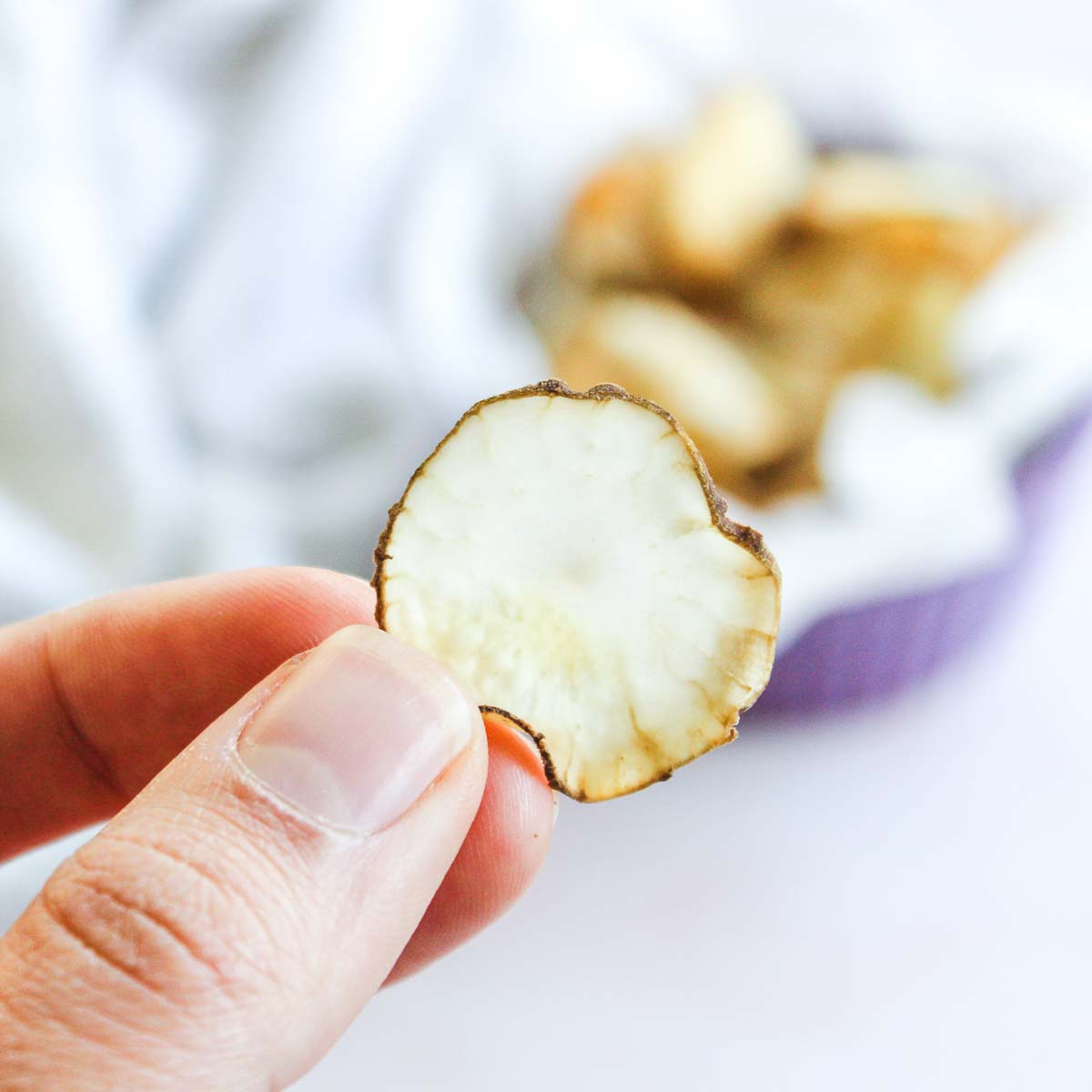 Hand holding crispy baked jerusalem artichoke chip.