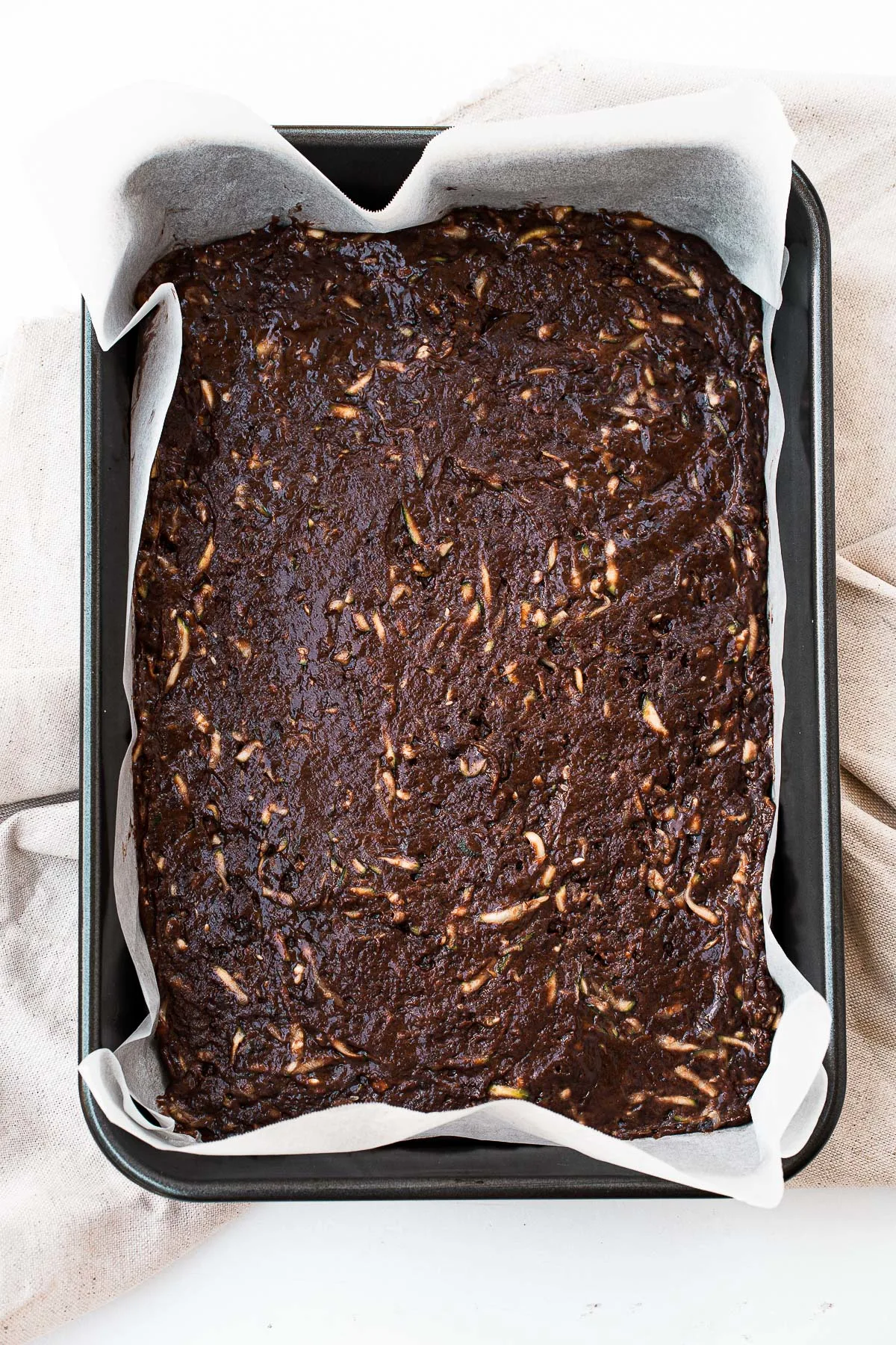 Brownie batter with zucchini in a baking dish.