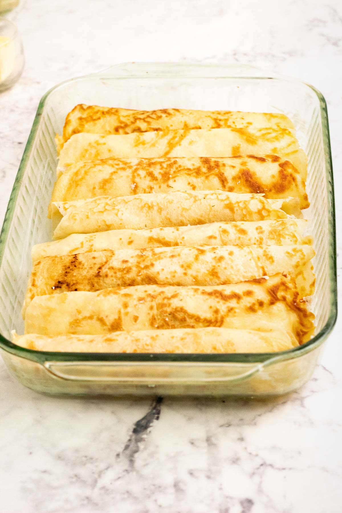 Rolled up chicken crepes in a baking pan. 