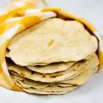 Stack of homemade flour tortillas wrapped in a towel.