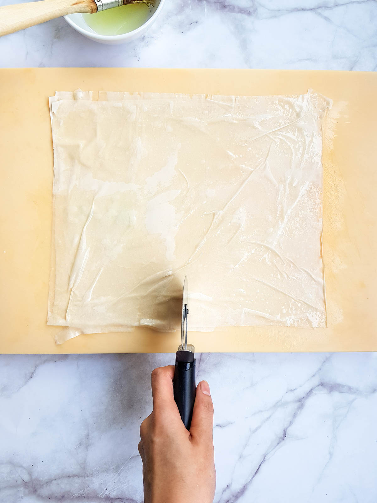 Slicing phyllo dough sheets brushed with oil.
