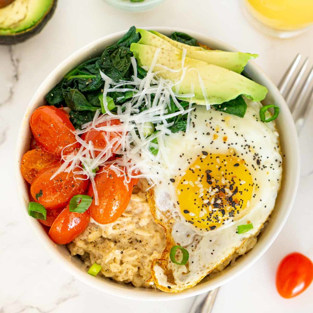 Bowl of savory oatmeal topped with fried egg, spinach, tomato, and avocado.