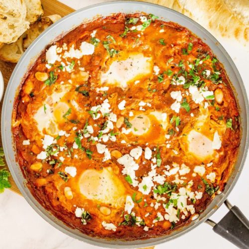 Shakshuka with feta and white beans in a skillet.