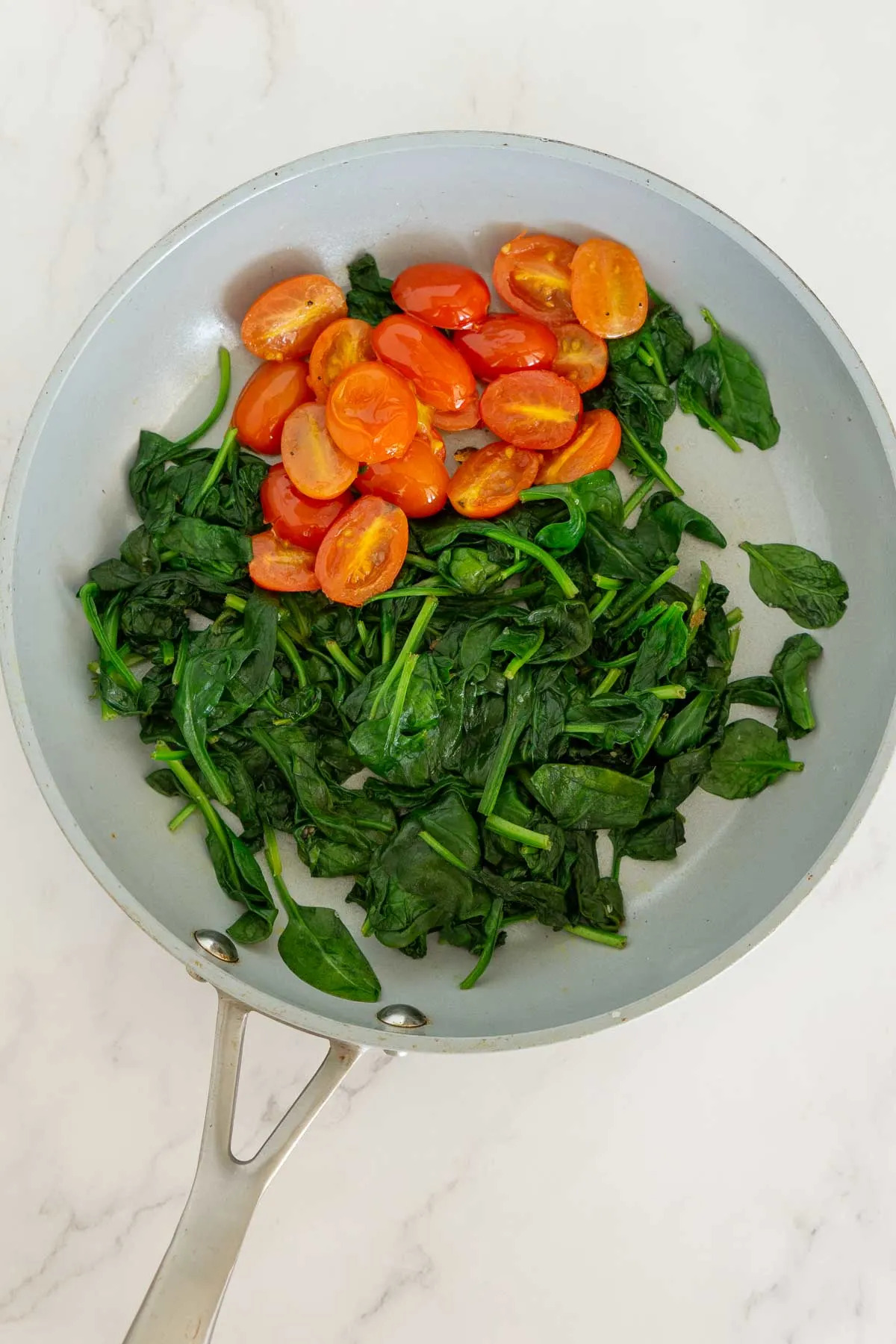 Sauteed spinach and grape tomatoes in a skillet.