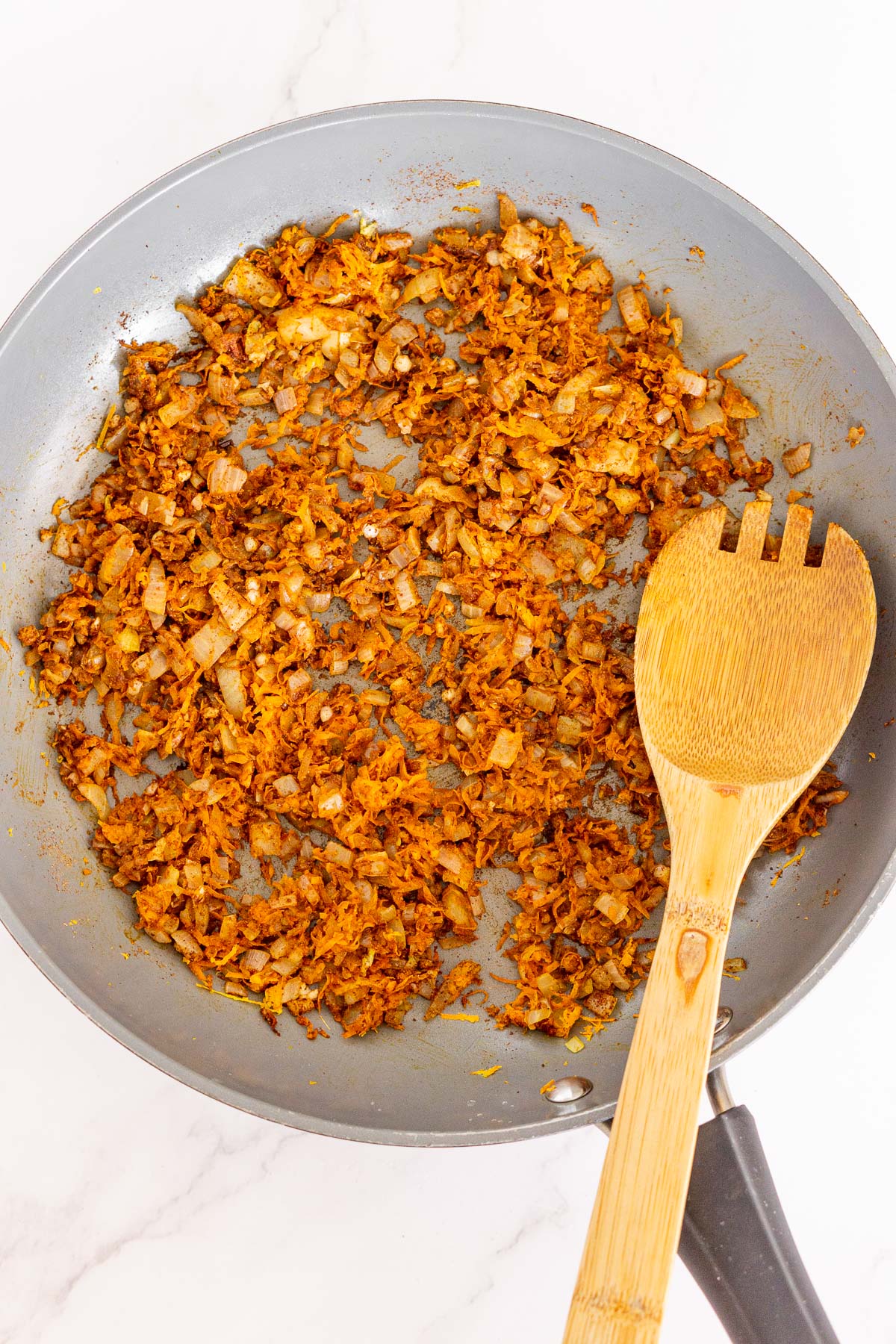 Sauteed carrots, onion, and shakshuka spices in a pan.
