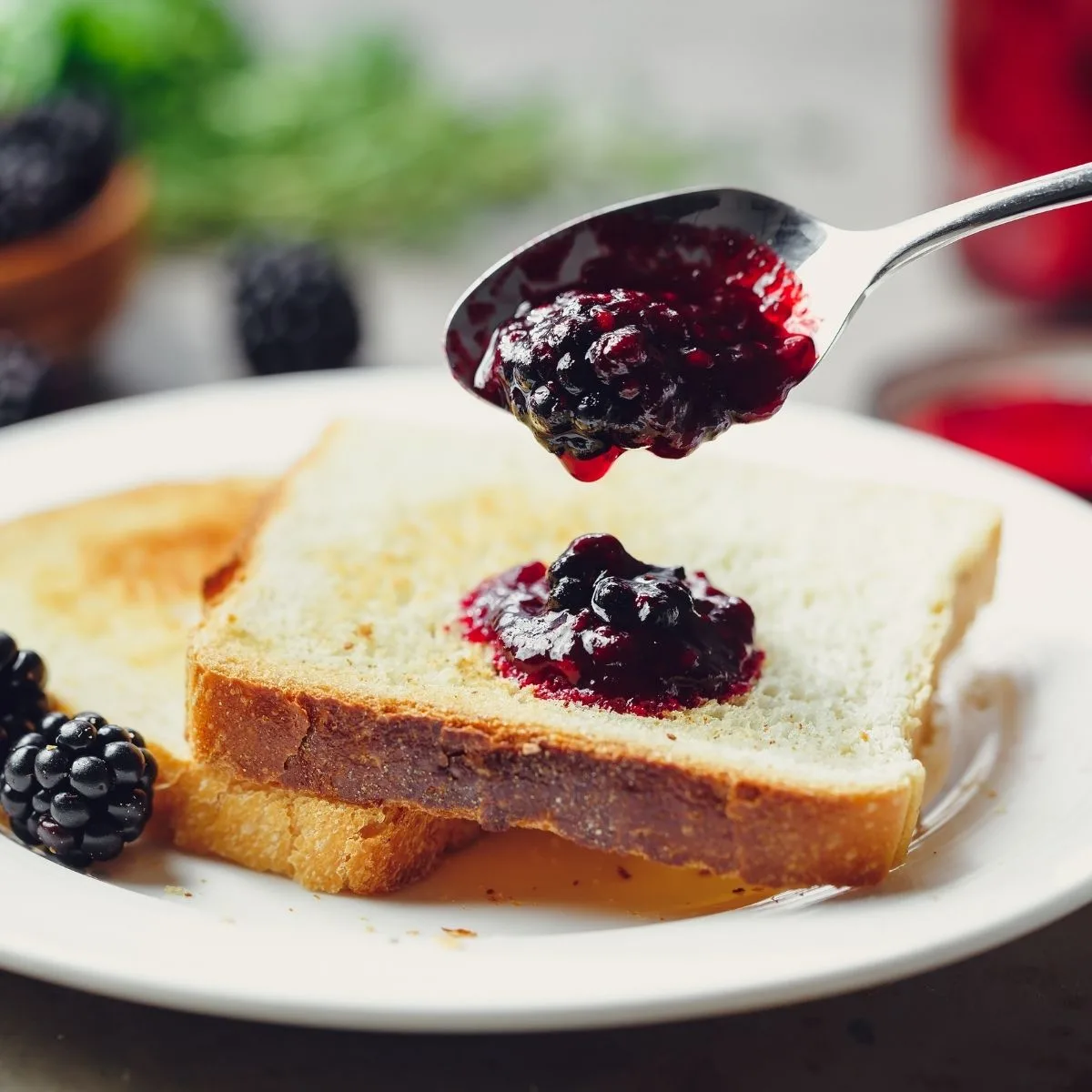 Spooning blackberry jam on toast.