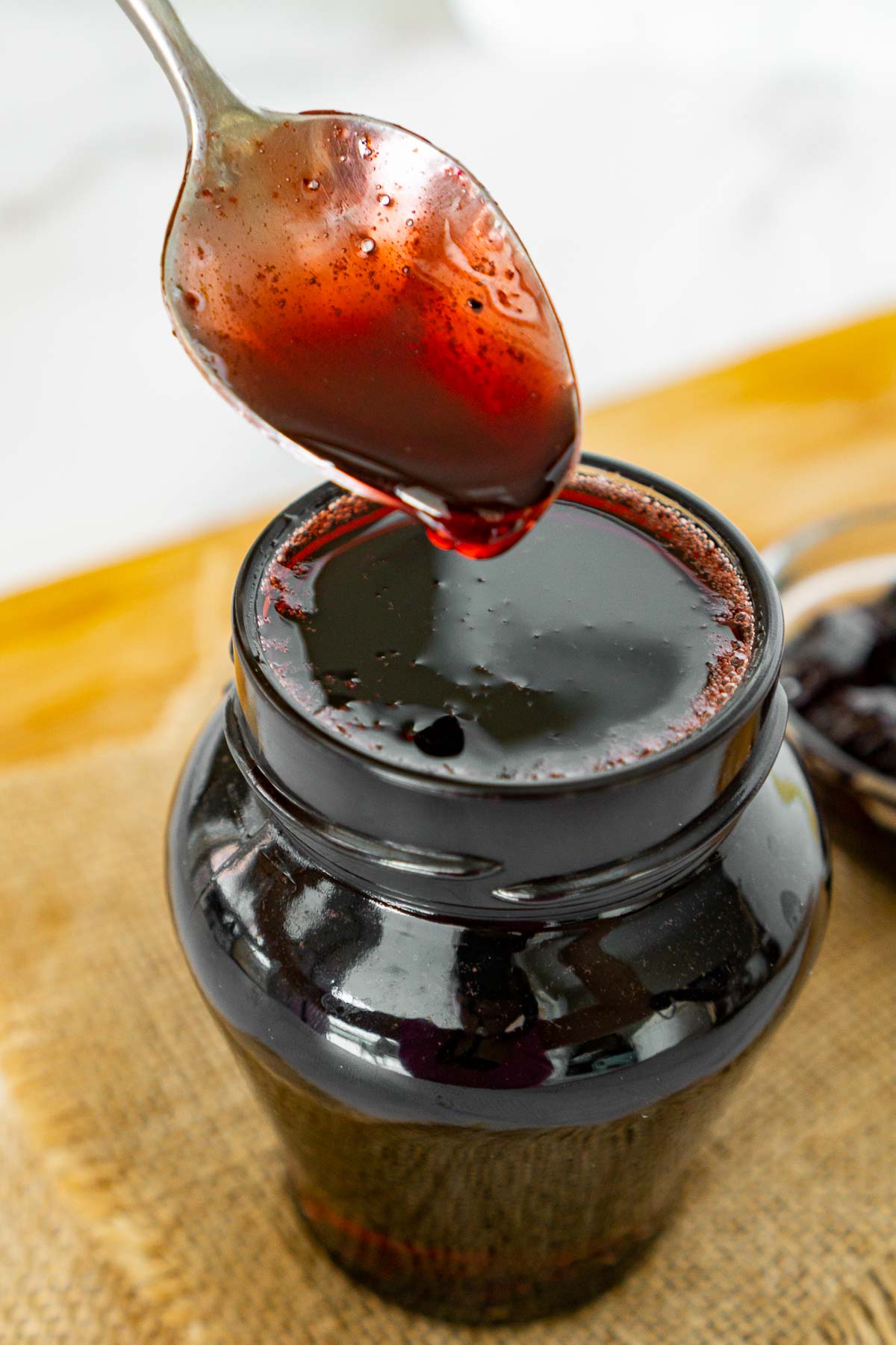 Cherry syrup on a spoon dripping into a jar.