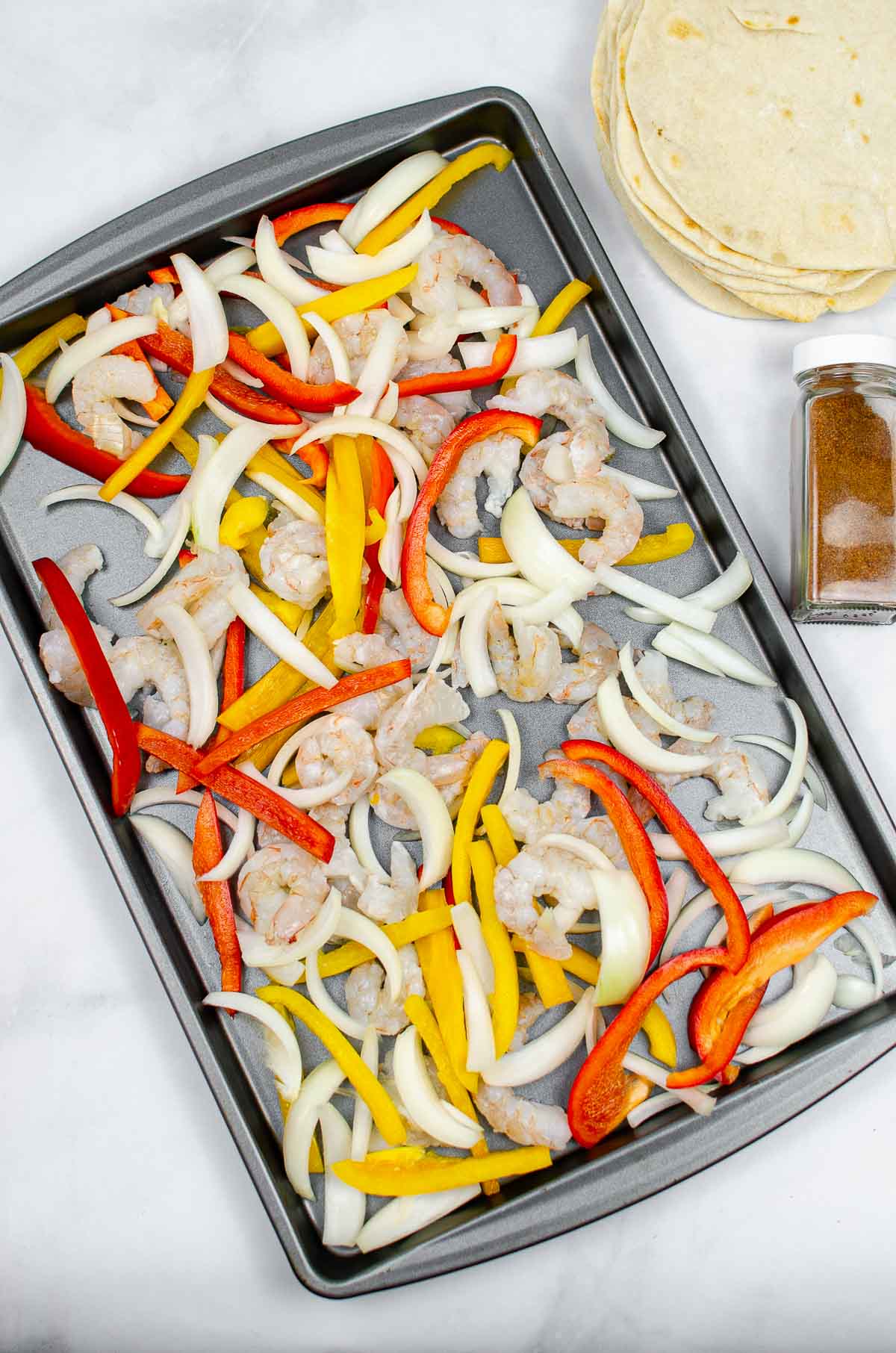 Sliced peppers, onions, and shrimp on a baking pan.