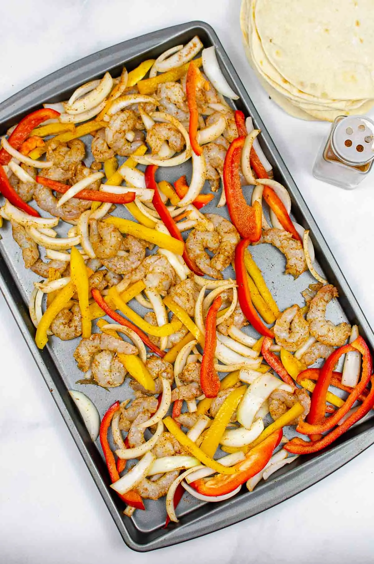Sliced peppers, onions, and shrimp seasoned with fajita seasoning on a sheet pan.