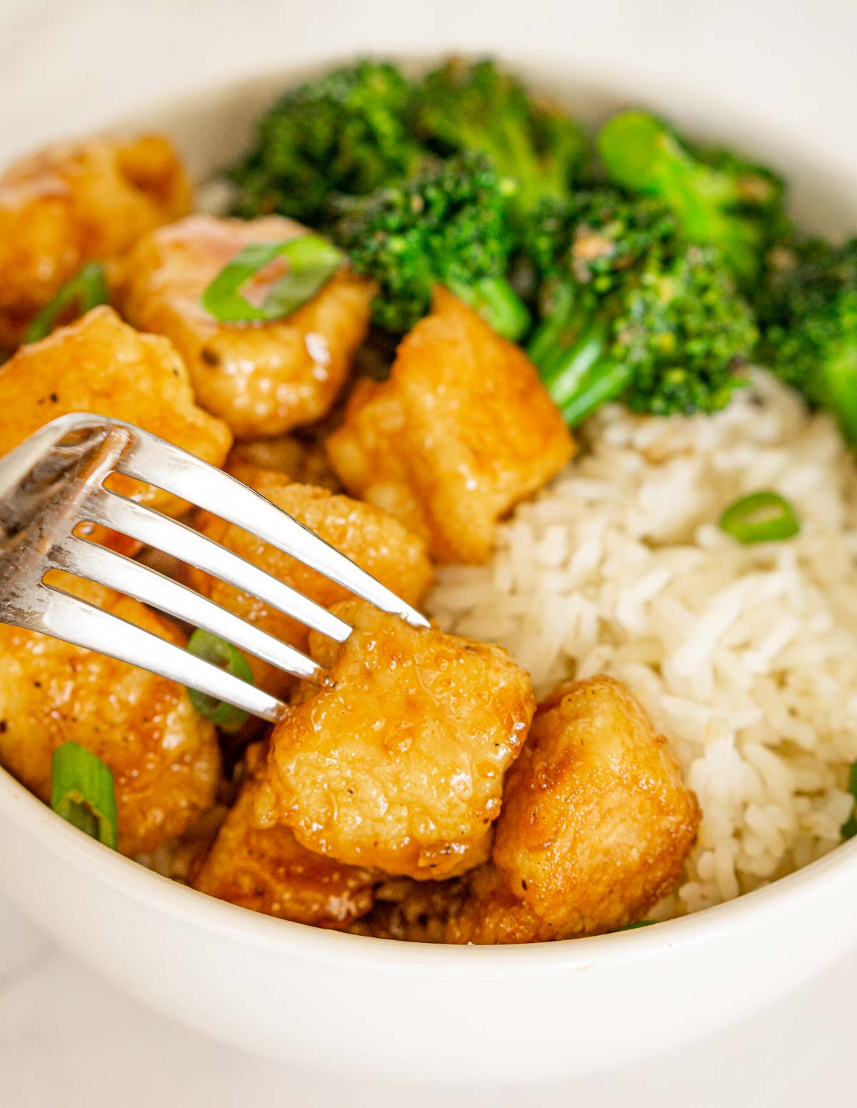 Fork grabbing a piece of hot honey chicken from a bowl of chicken, rice, and broccoli.