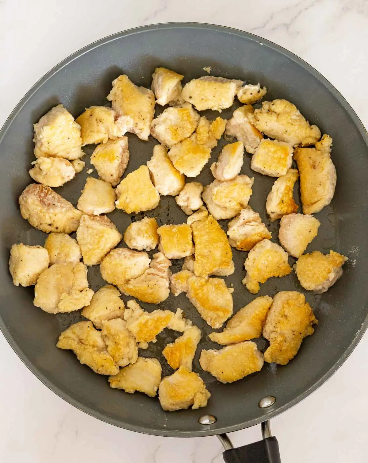 Skillet with cooked cubed chicken.
