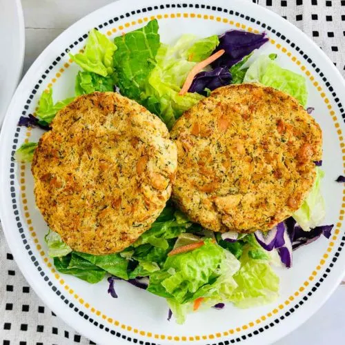 Two salmon potato patties over salad on a plate.