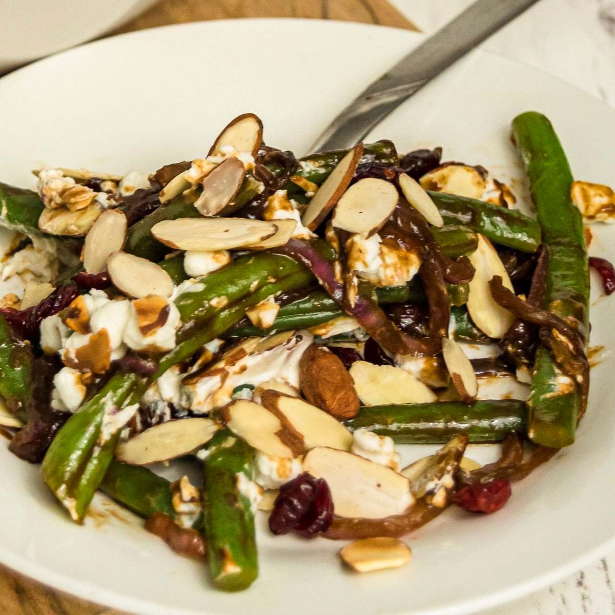 Plate of green beans with sliced almonds, dried cranberries, and balsamic sauce.