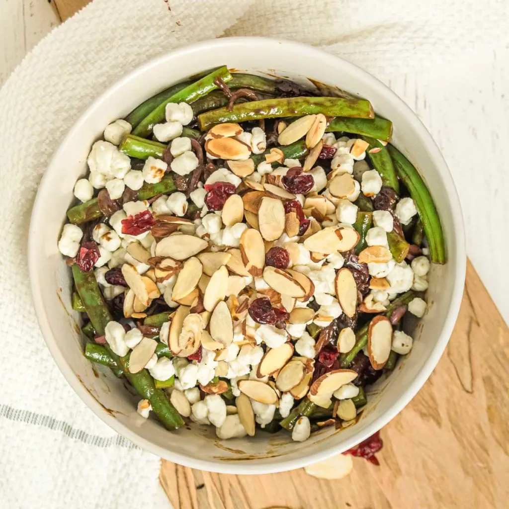 Bowl of green beans with balsamic sauce, almonds, and cranberries.