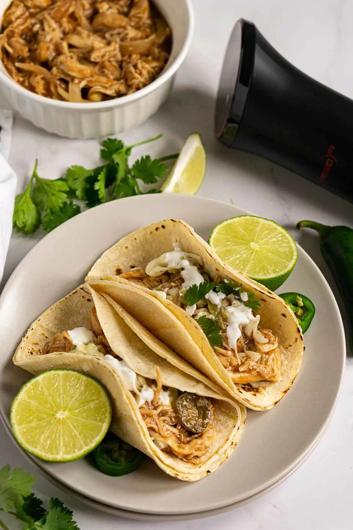 Shredded chicken tacos on a plate next to sous vide cooker