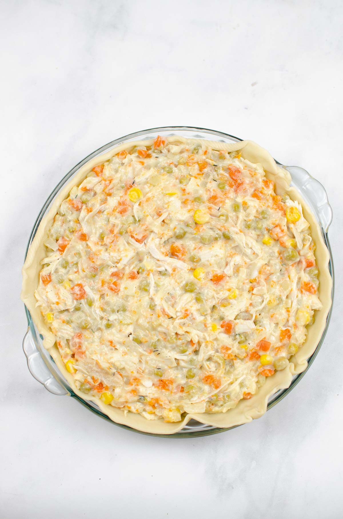 Uncooked turkey pot pie with filling in a pie dish.