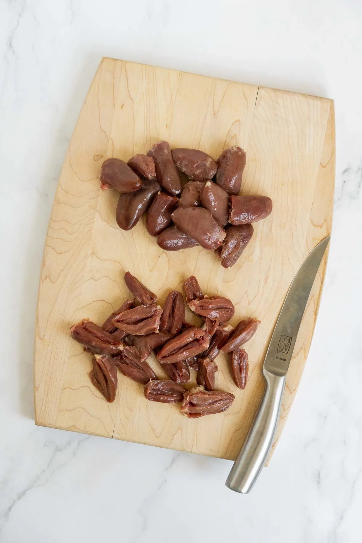 Sliced chicken hearts on a cutting board.