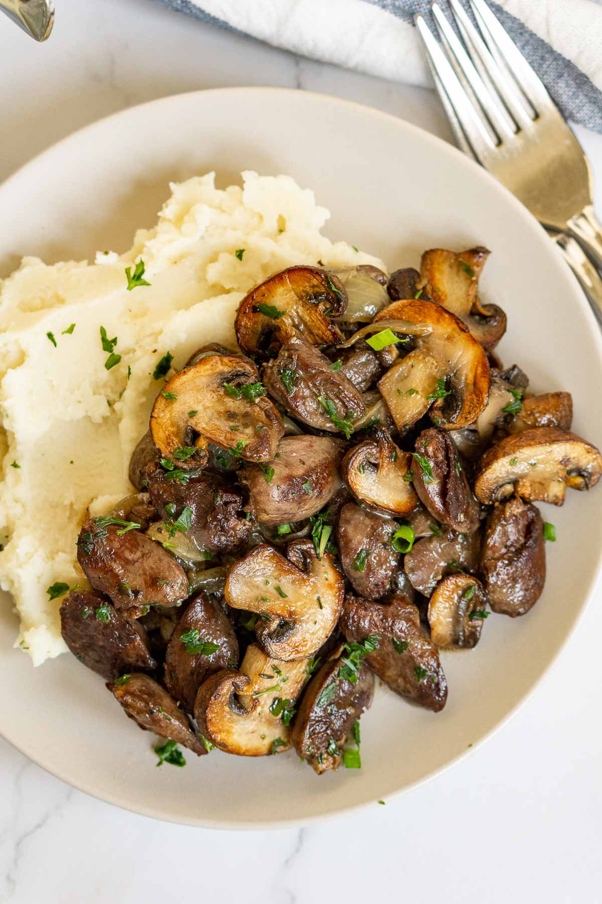 Chicken hearts with sauteed mushrooms and mashed potatoes on a plate.