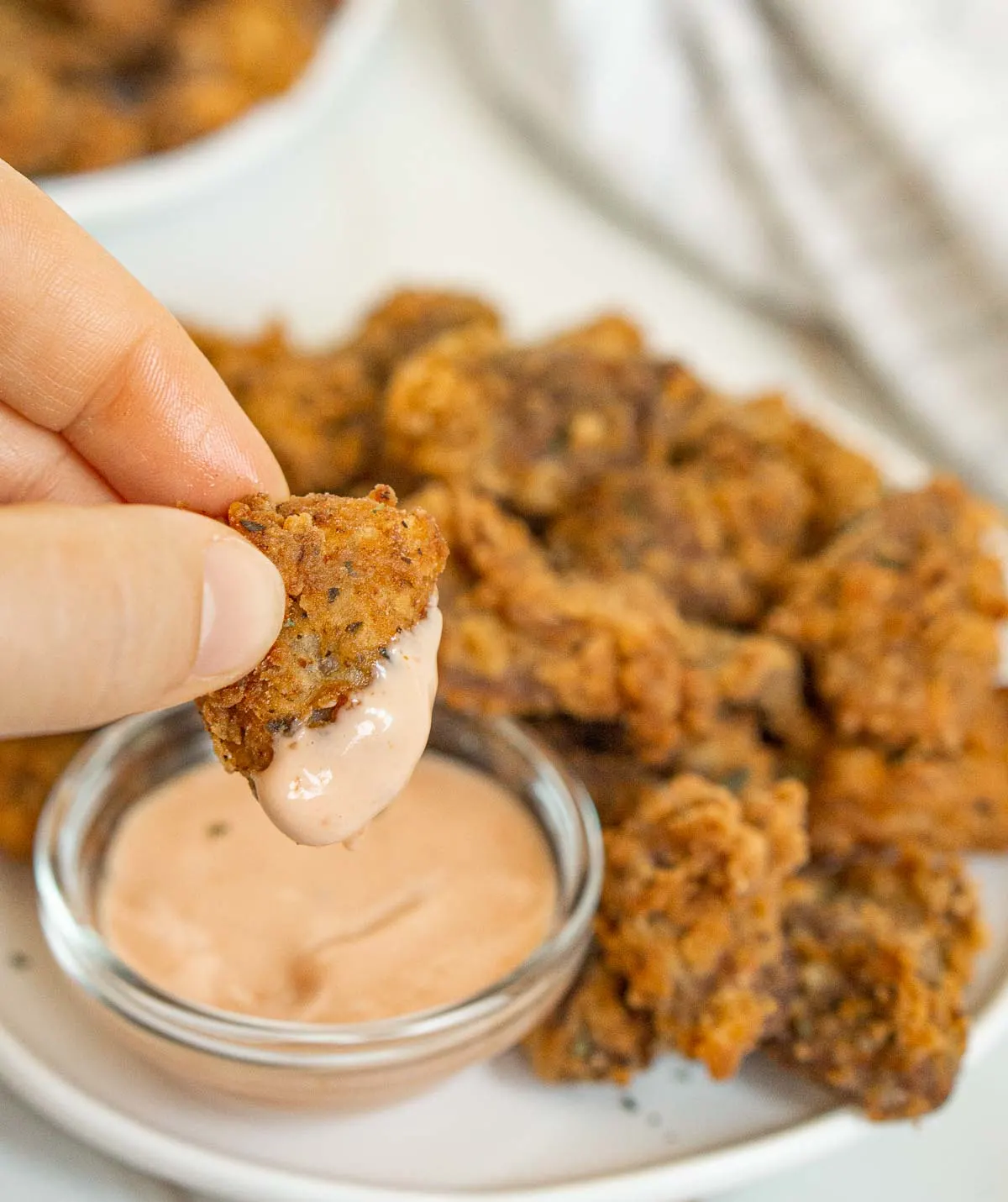 Hand dipping fried chicken heart into ketchup and mayo sauce.