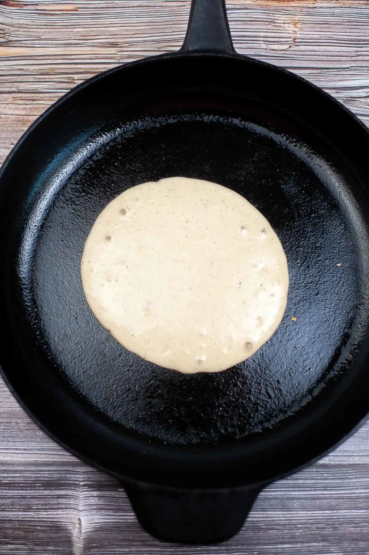 A pancake cooking in a skillet with bubbles forming.