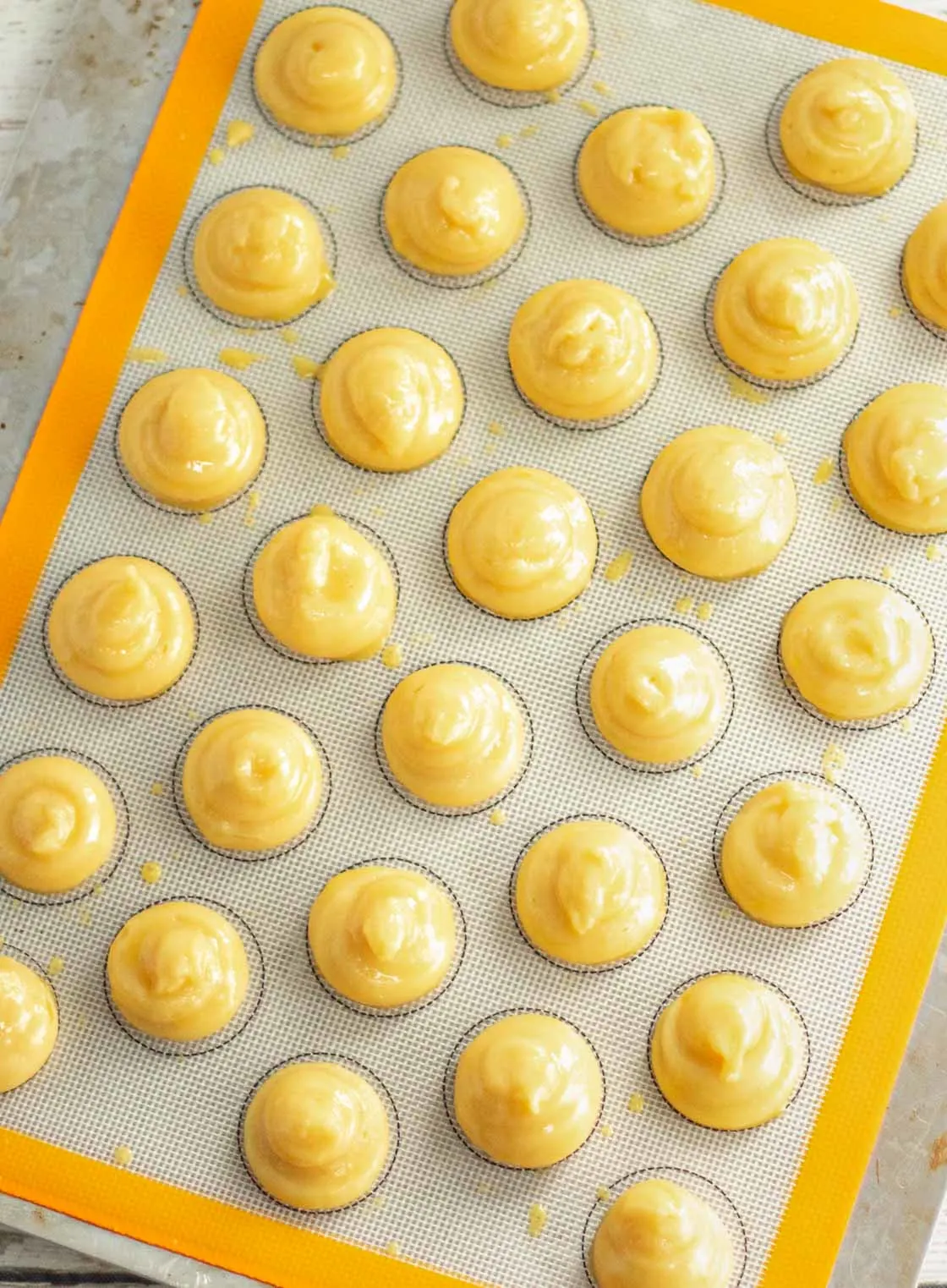 Cream puff dough piped in circles on a silicone baking mat.