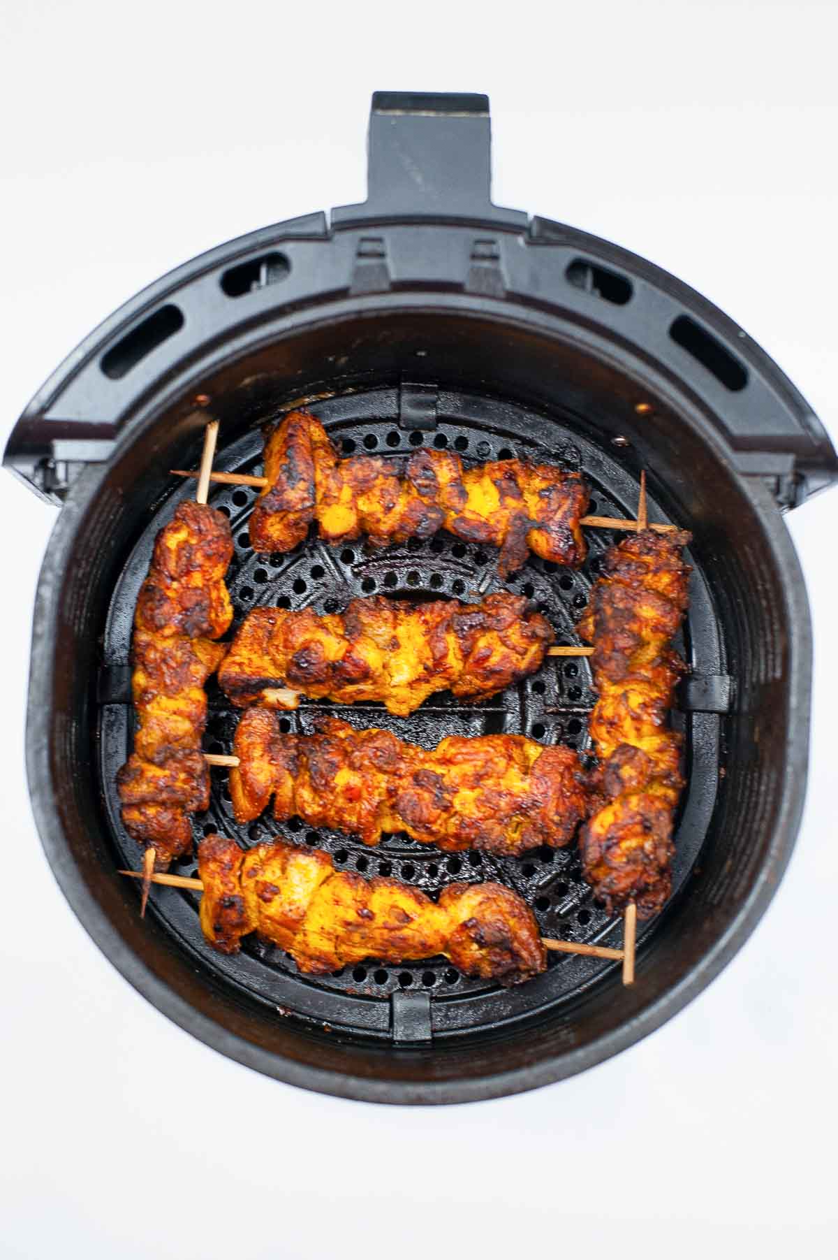 Cooked tandoori chicken kebabs in an air fryer.