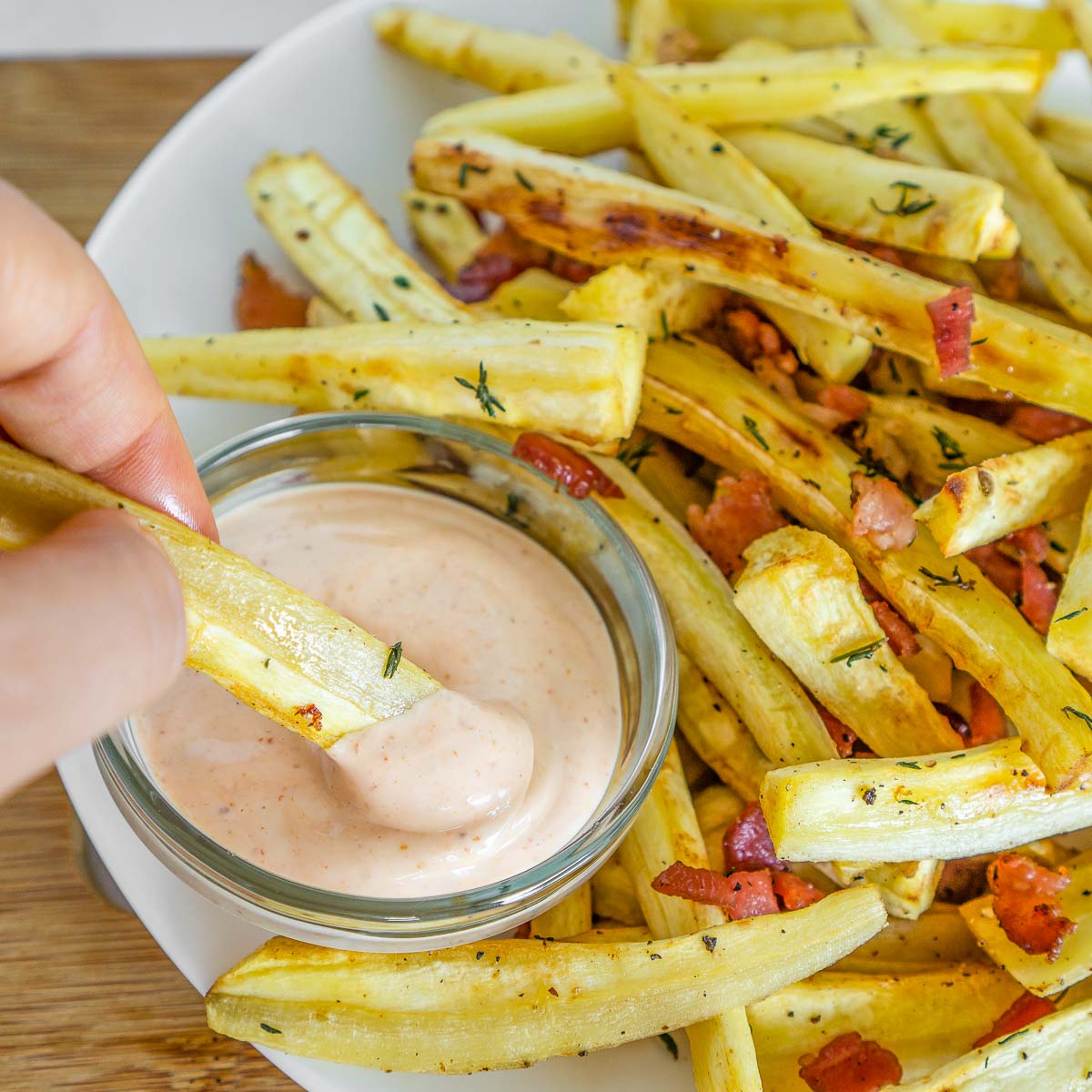 Hand dipping roasted parsnips into spicy mayo