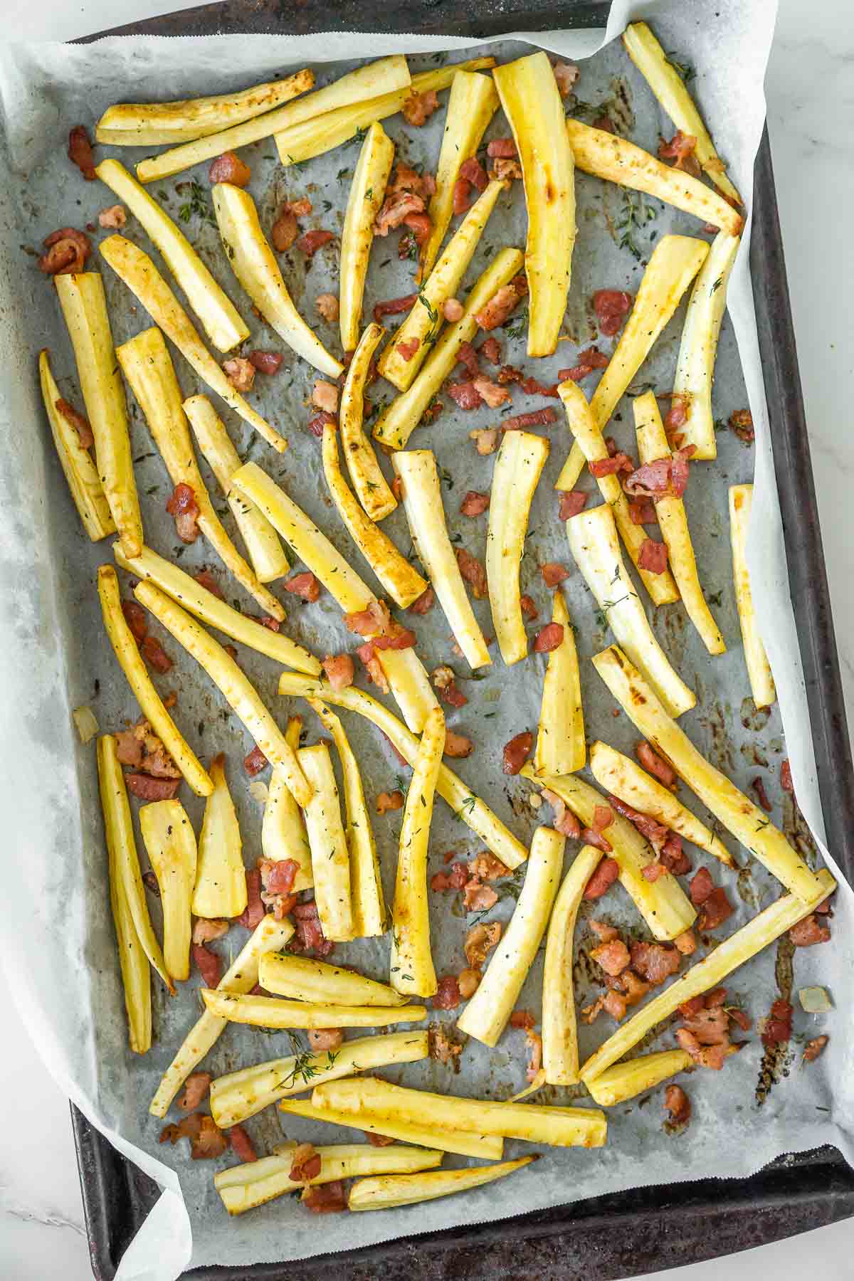 Baking sheet with parsnip fries and crispy bacon bits.