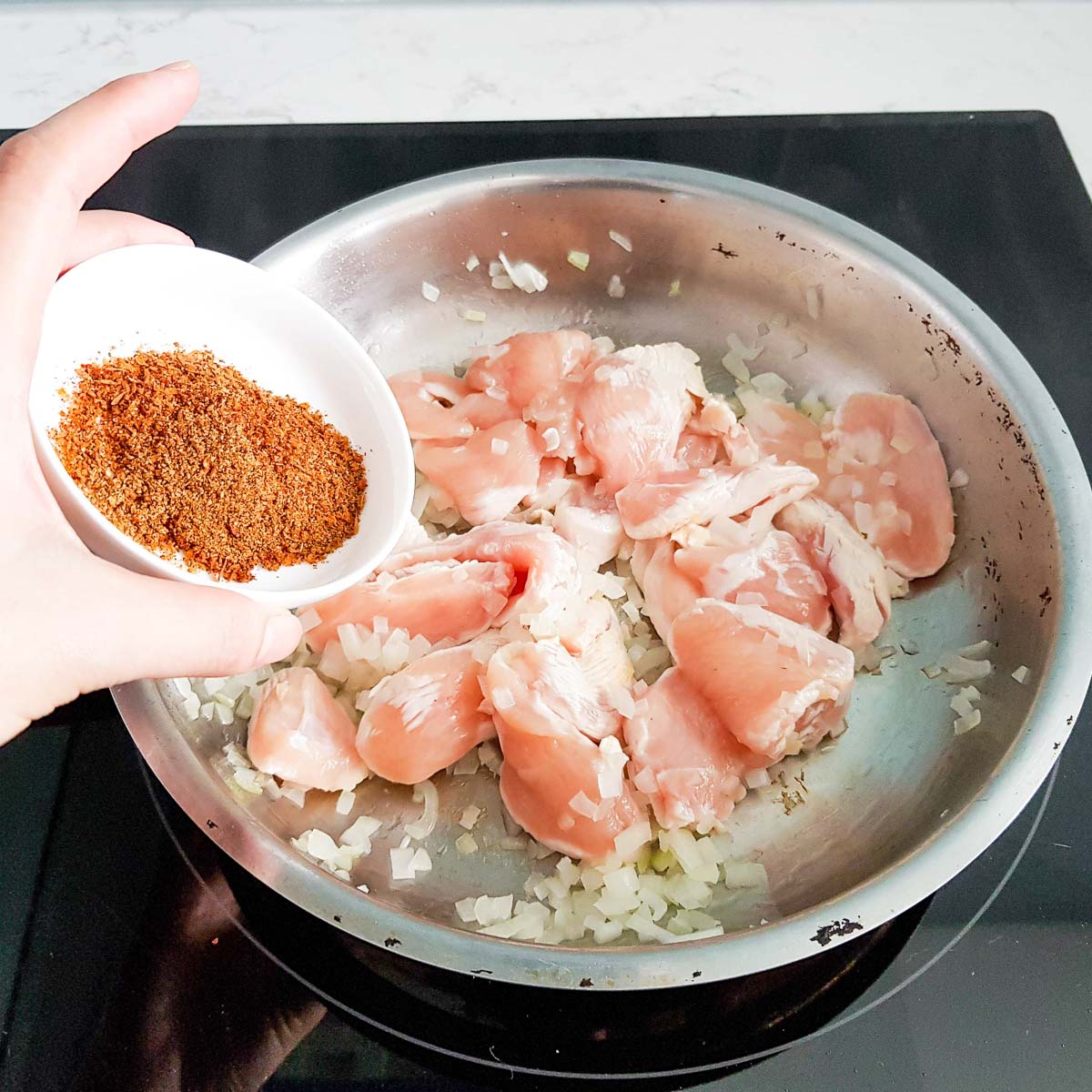 Adding Cajun seasoning to diced chicken in a pan.
