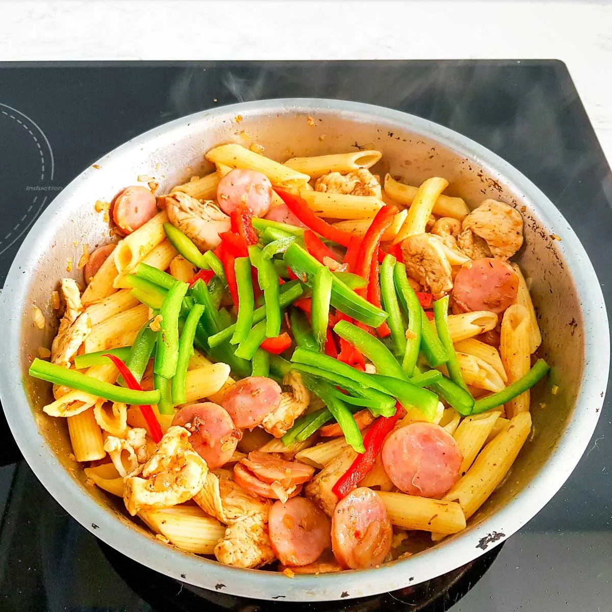 Adding bell peppers to creamy cajun chicken pasta in a skillet.