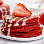 Stack of red velvet pancakes with cream cheese glaze and strawberries on top/