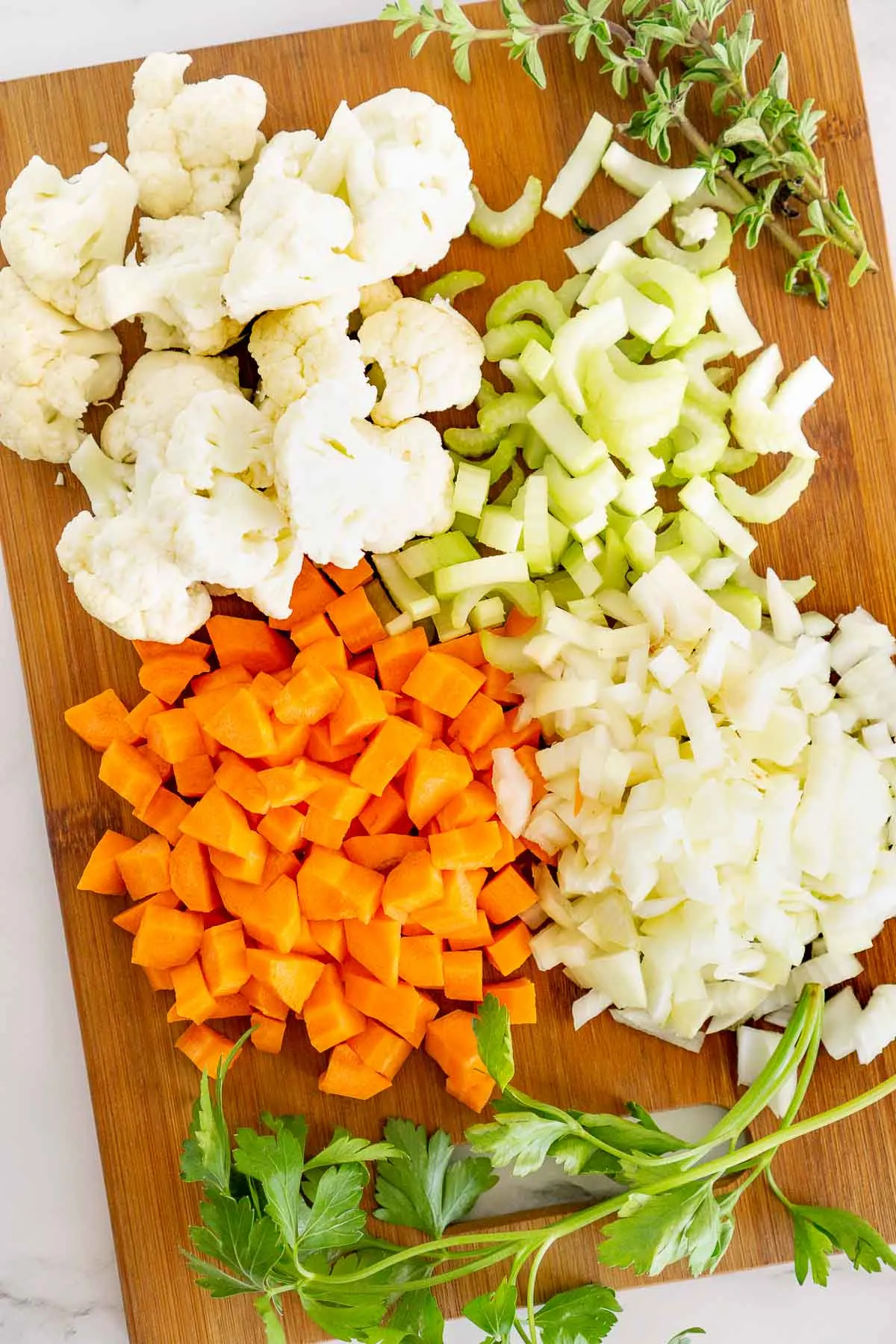 Chopped carrots, celery, onion, and cauliflower on a cutting board.