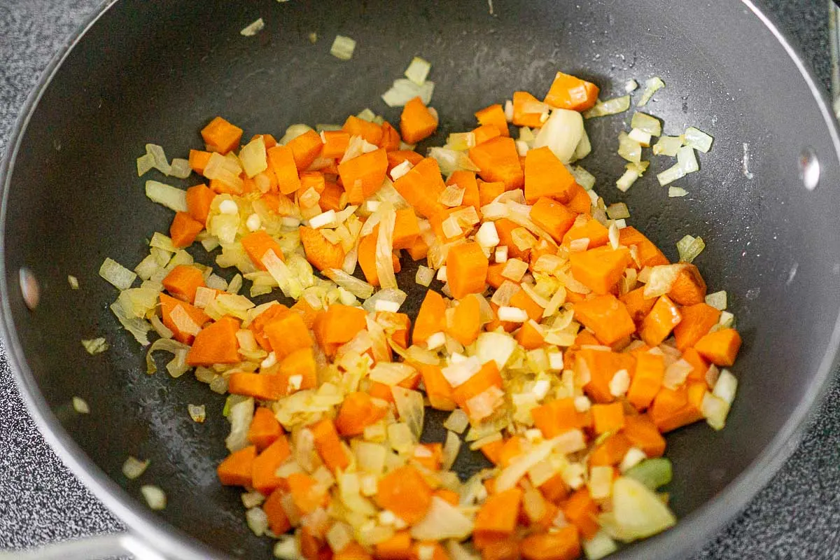 Sautéing carrots and onions in a soup pot.
