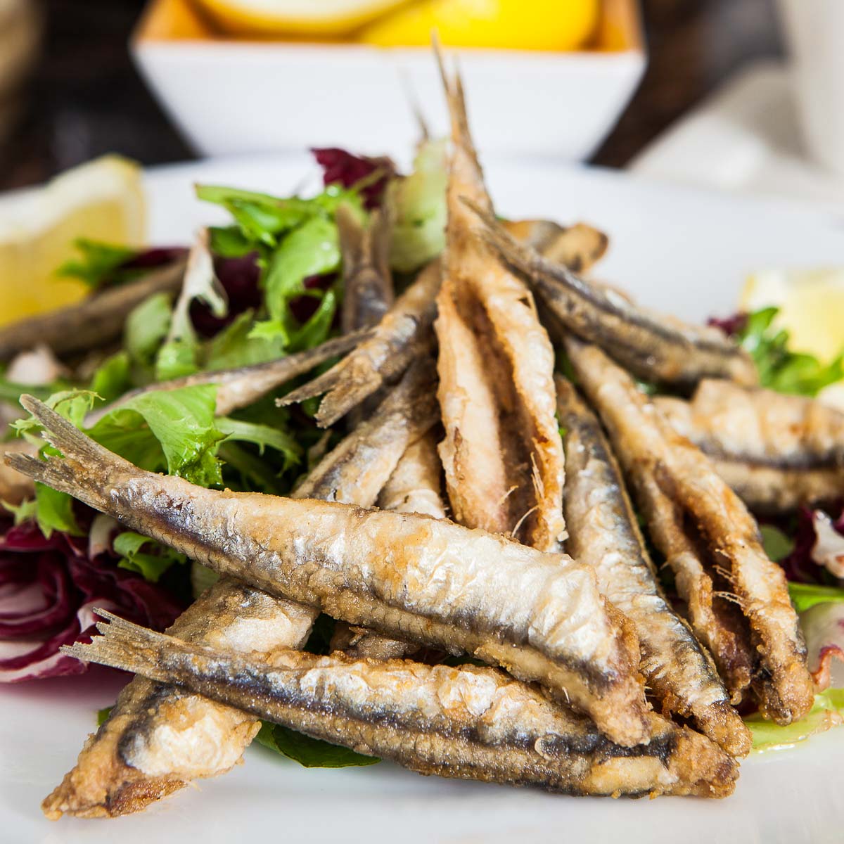 Plate of crispy fried anchovies over salad.