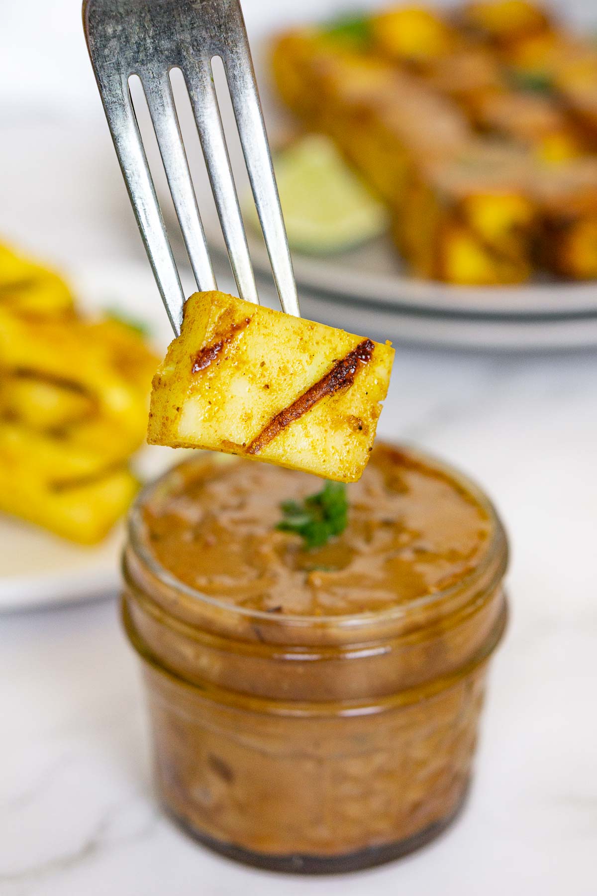 Dipping piece of grilled paneer into peanut sauce