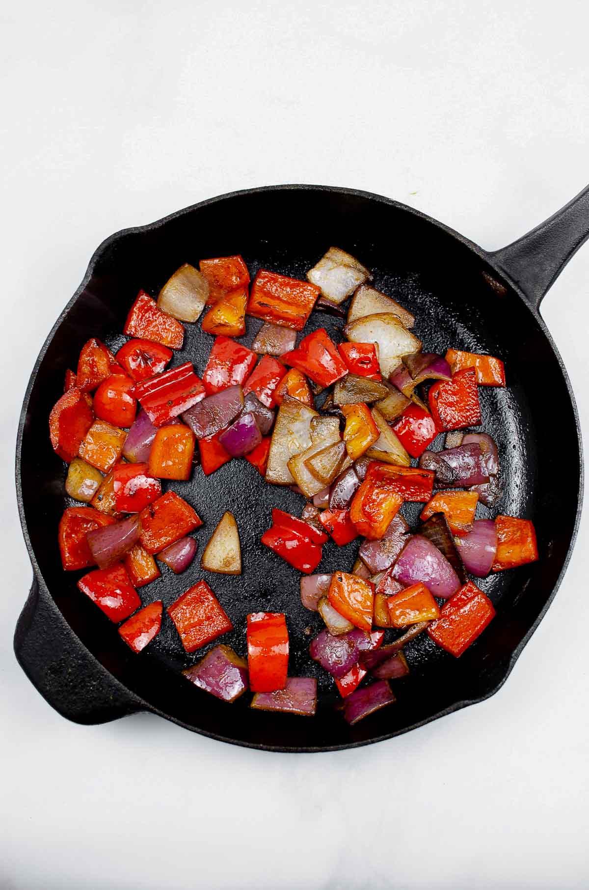 Bell peppers and onions sautéing in a cast iron skillet
