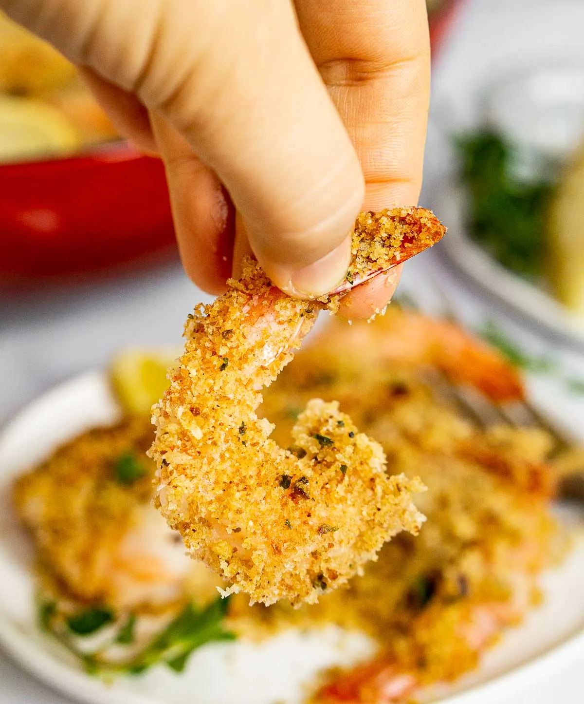 Hand holding piece of crispy shrimp oreganata by the tail.