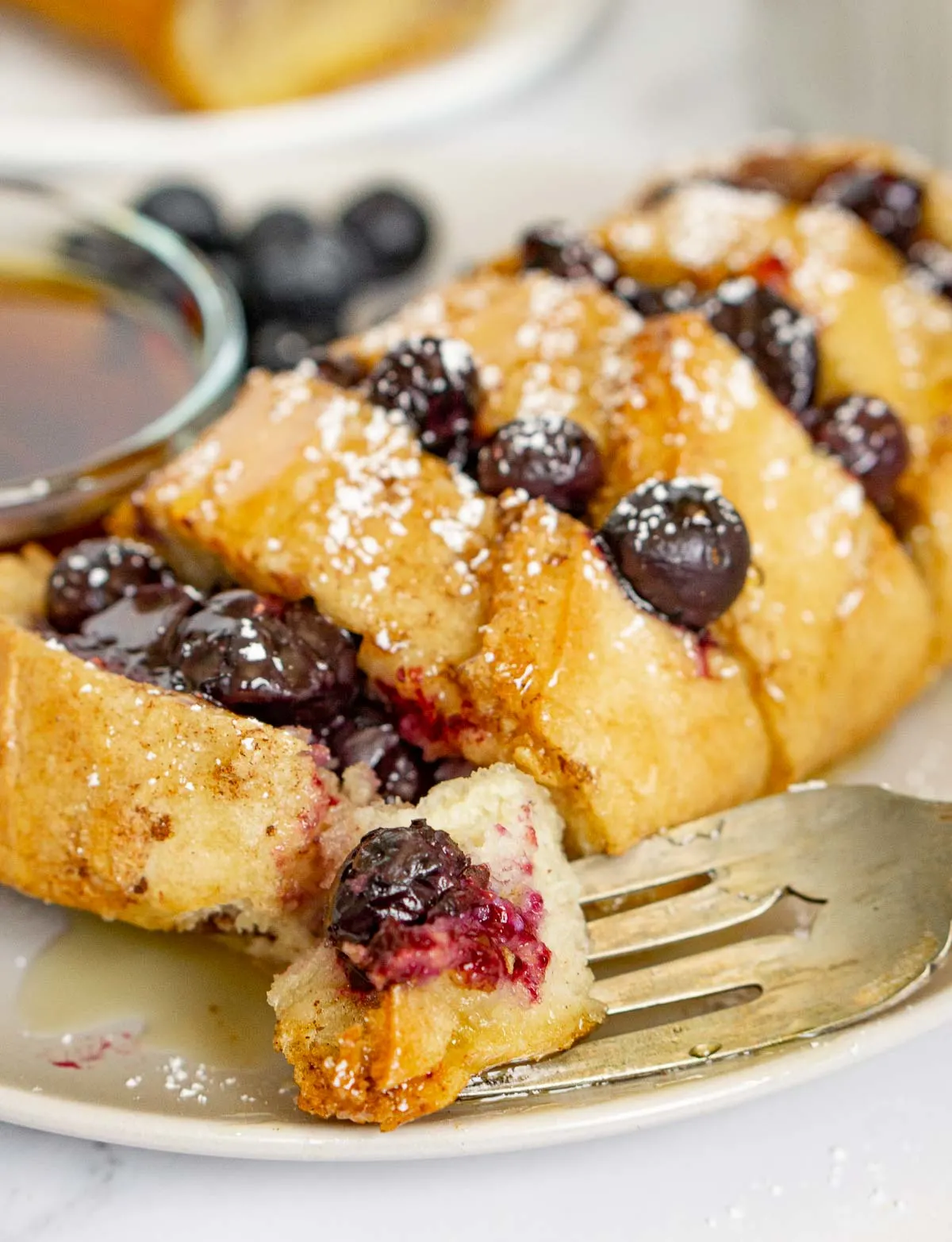 Fork with a piece of baked baguette French toast with blueberries