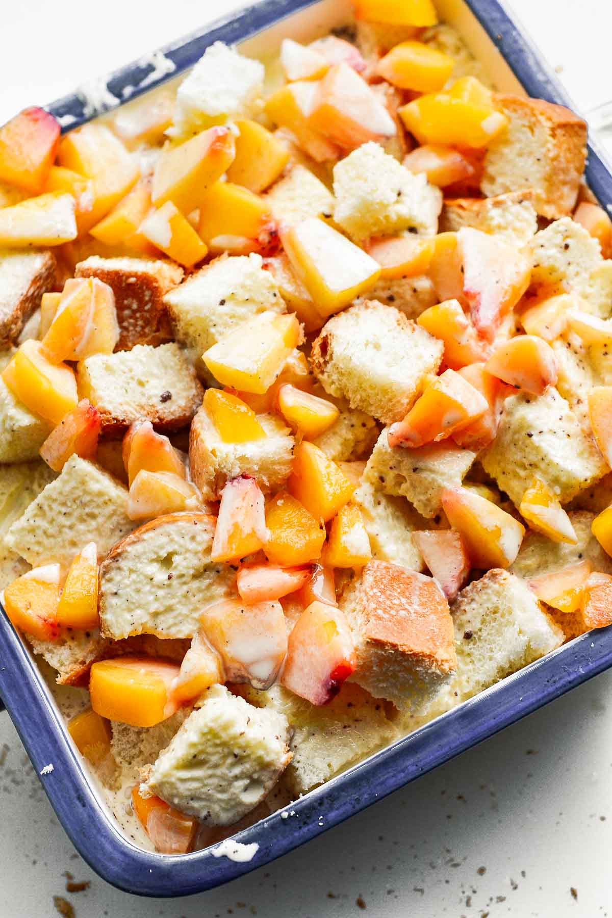 Cubed bread and diced peaches in a baking pan with milk and egg mixture poured on top