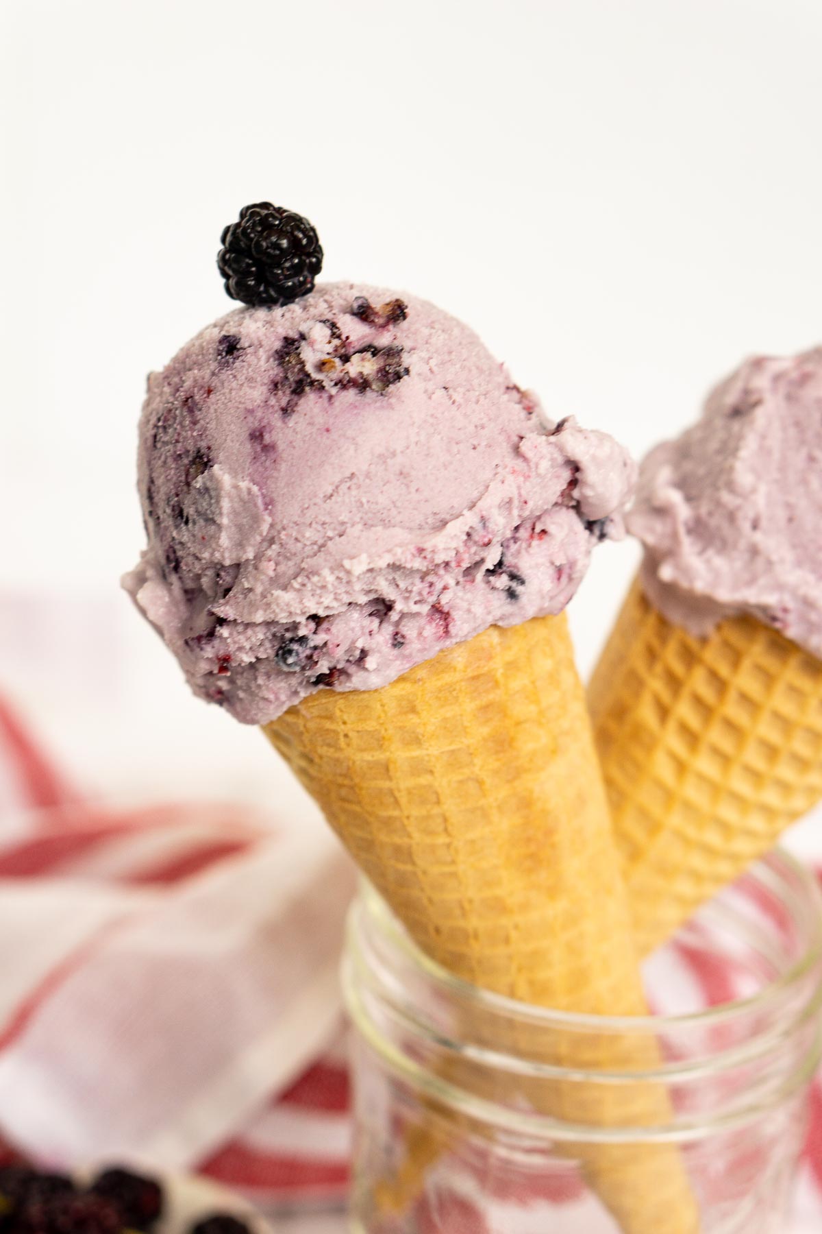 Close up of mulberry ice cream cone garnished with a fresh mulberry