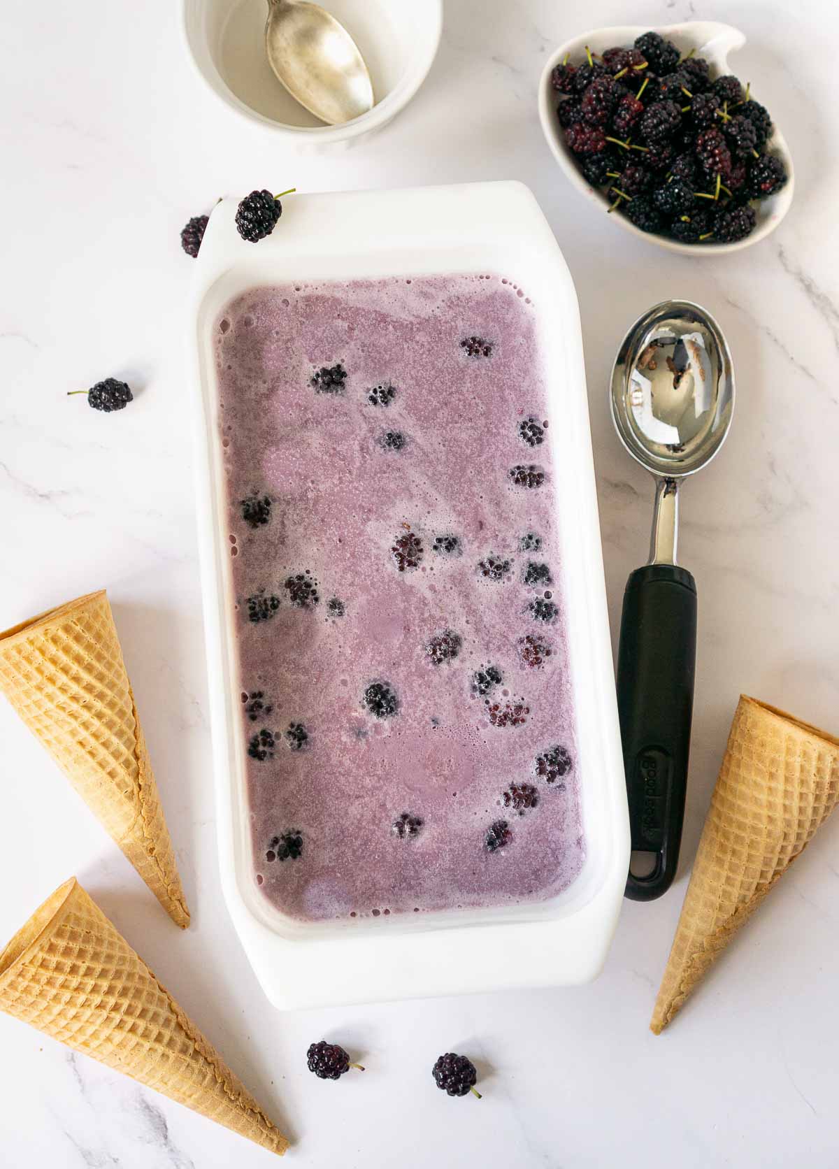 Mulberry ice cream in a freezer container with mulberry garnish on the side